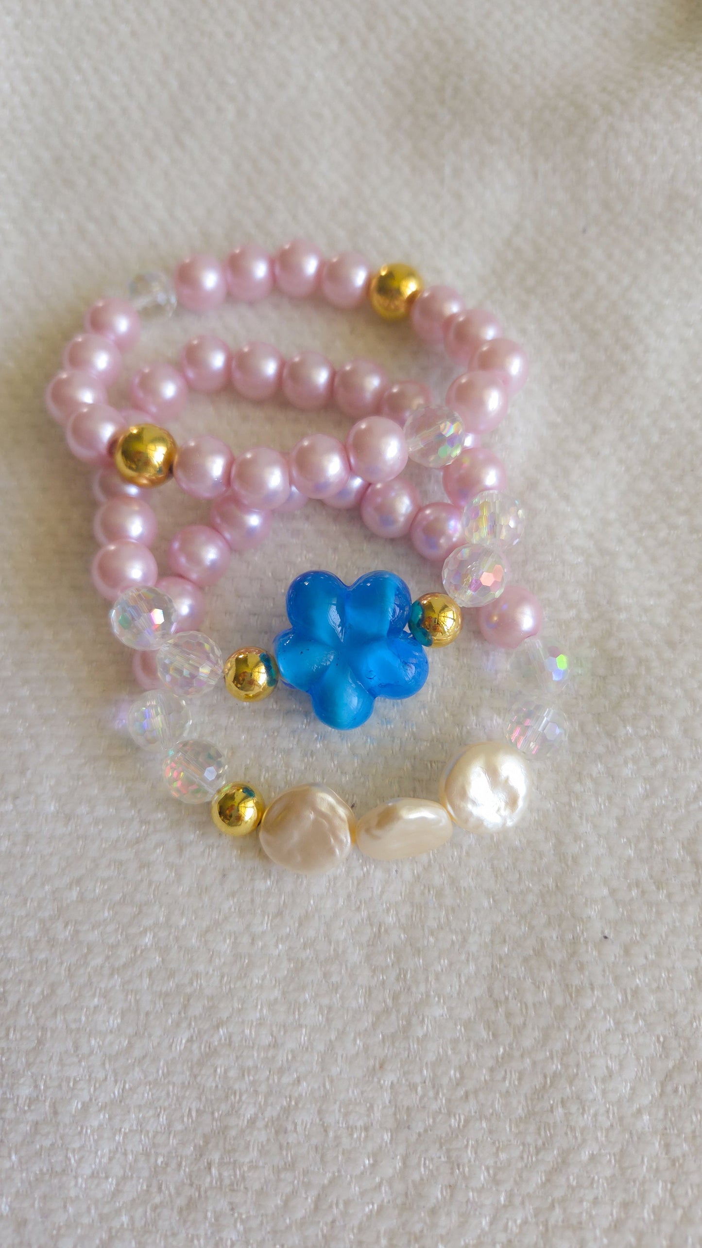 Pearl necklace with a blue flower pendant on a textured surface