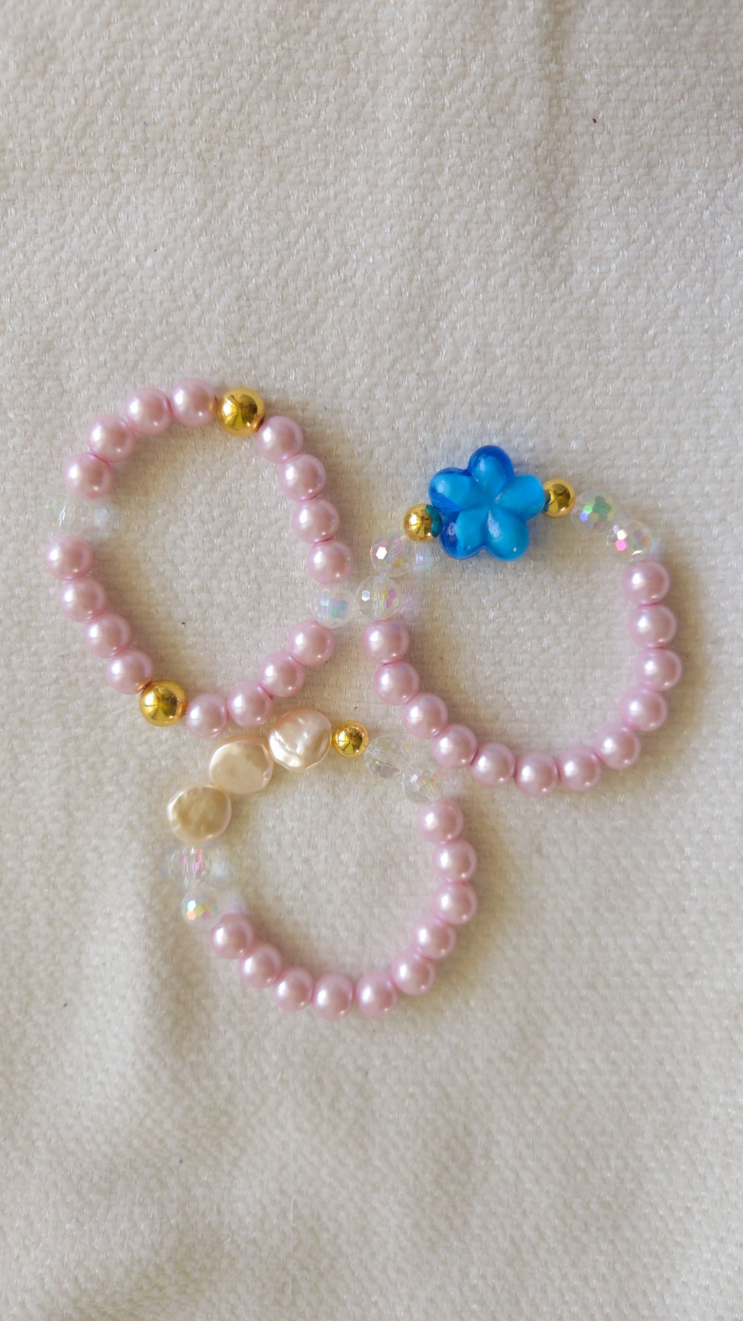Two pink beaded bracelets with blue flower charm on a beige background
