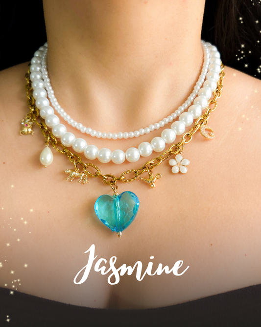 Close-up of a Jasmine-inspired charm necklace with layered glass pearls, gold chain, blue heart pendant, and magical elements like a tiger, flower, moon, and lamp.