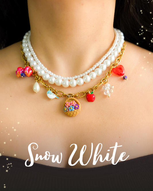 Close-up of a three-layer Snow White inspired necklace featuring pearls, a golden chain, and themed charms like a poison apple, singing bird, flower basket, and red heart. Worn on a model's neck.